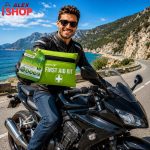 Bajker pokazuje kompaktan komplet prve pomoći pored motocikla na obalskom putu.